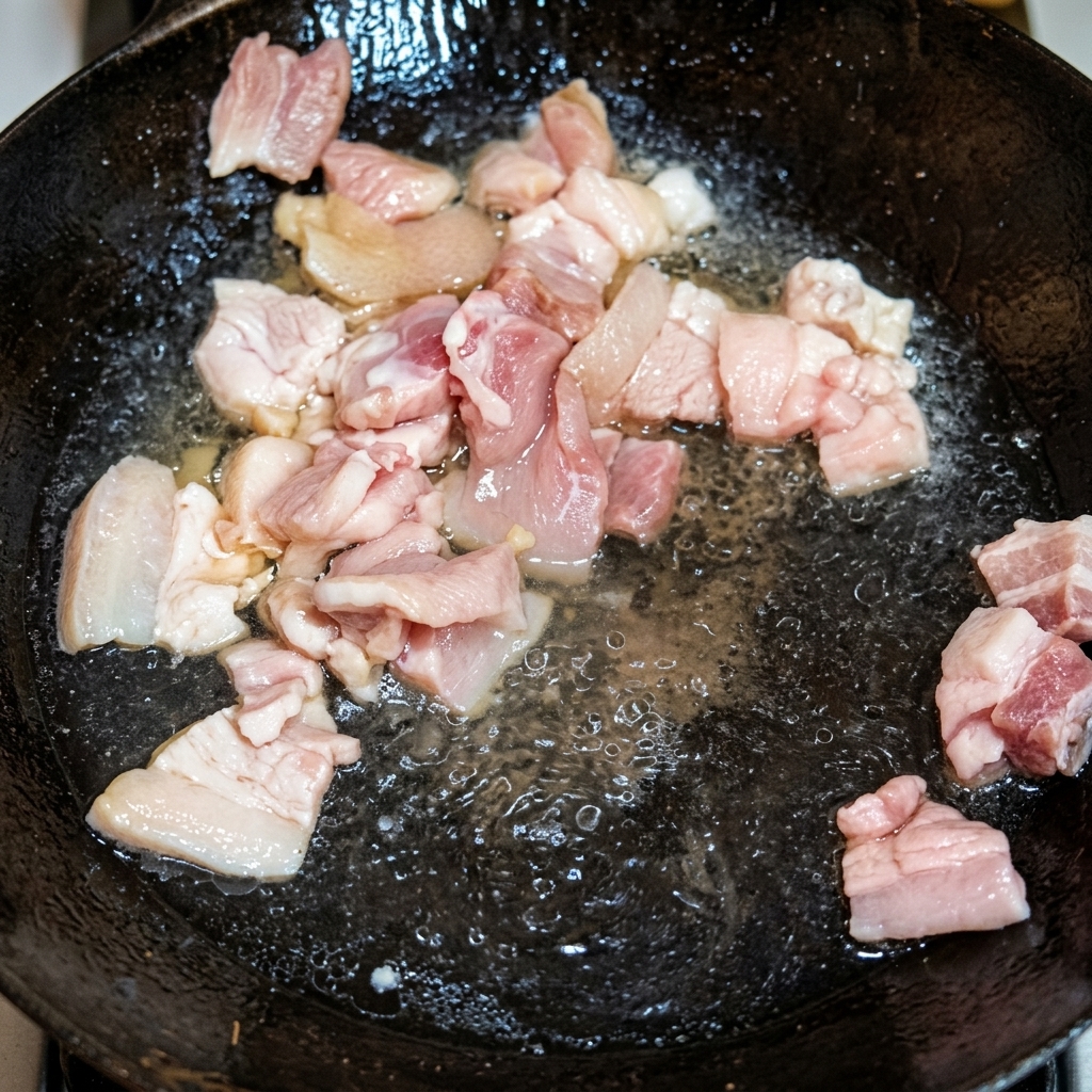 Trozos de panceta dorándose en manteca de cerdo dentro de un wok tradicional.