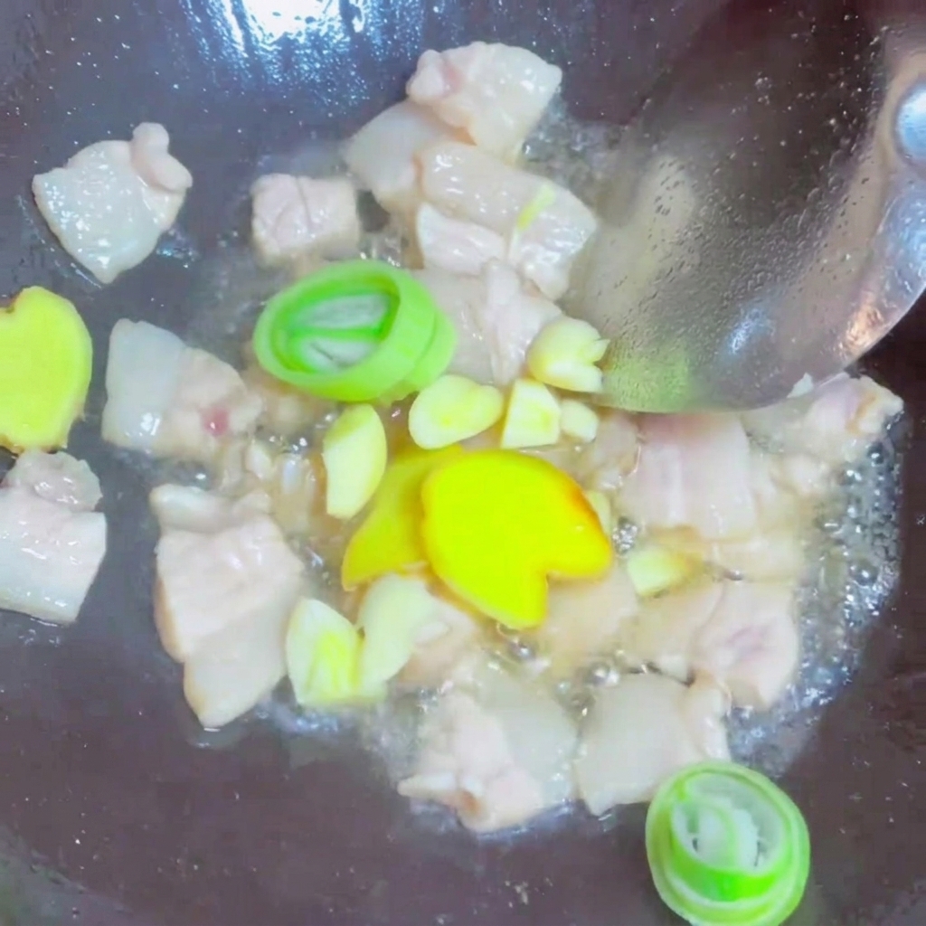Rodajas de jengibre fresco, ajo y cebolletas mezclándose con el cerdo frito en un wok.