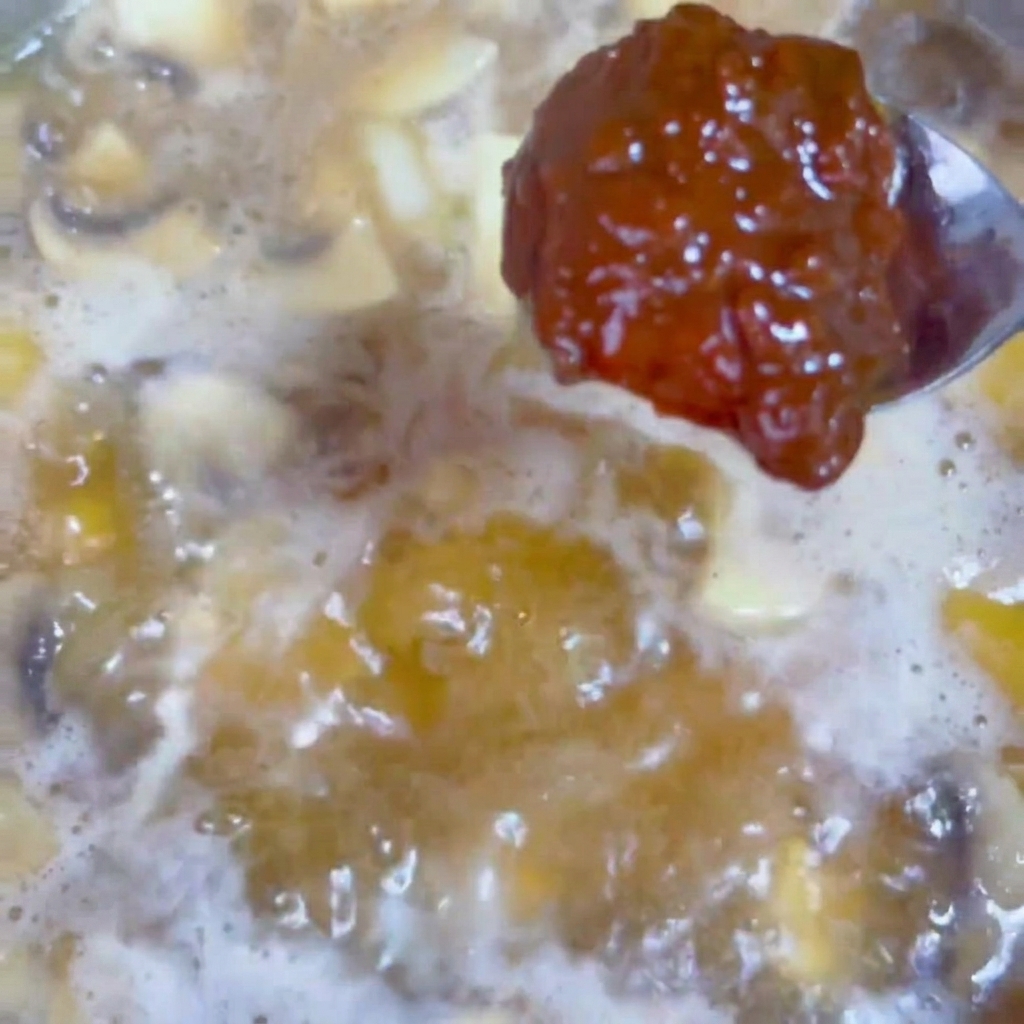 Una cucharada de pasta de soja oscura mezclándose en un caldo burbujeante dentro de un wok.