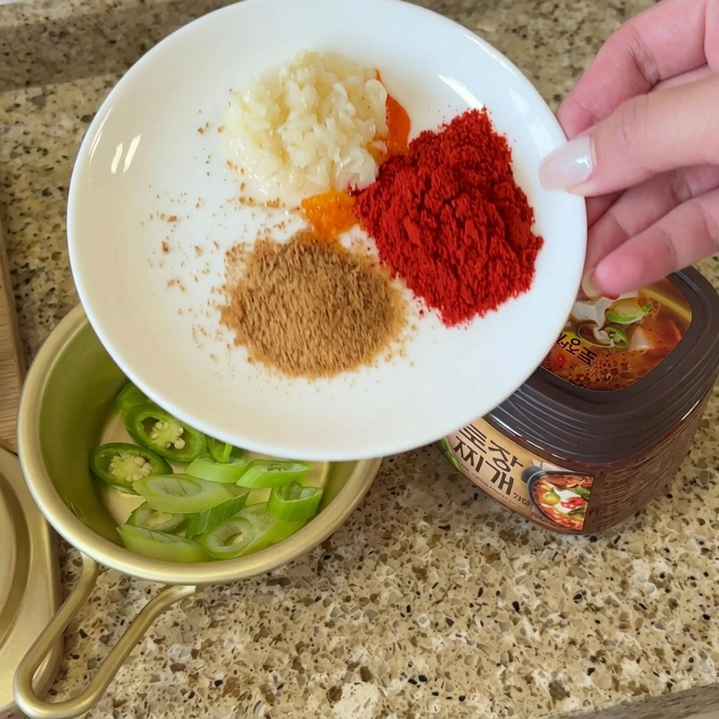 Un plato con porciones de ajo picado, chile en polvo, caldo de ternera y polvo de perilla junto al doenjang.