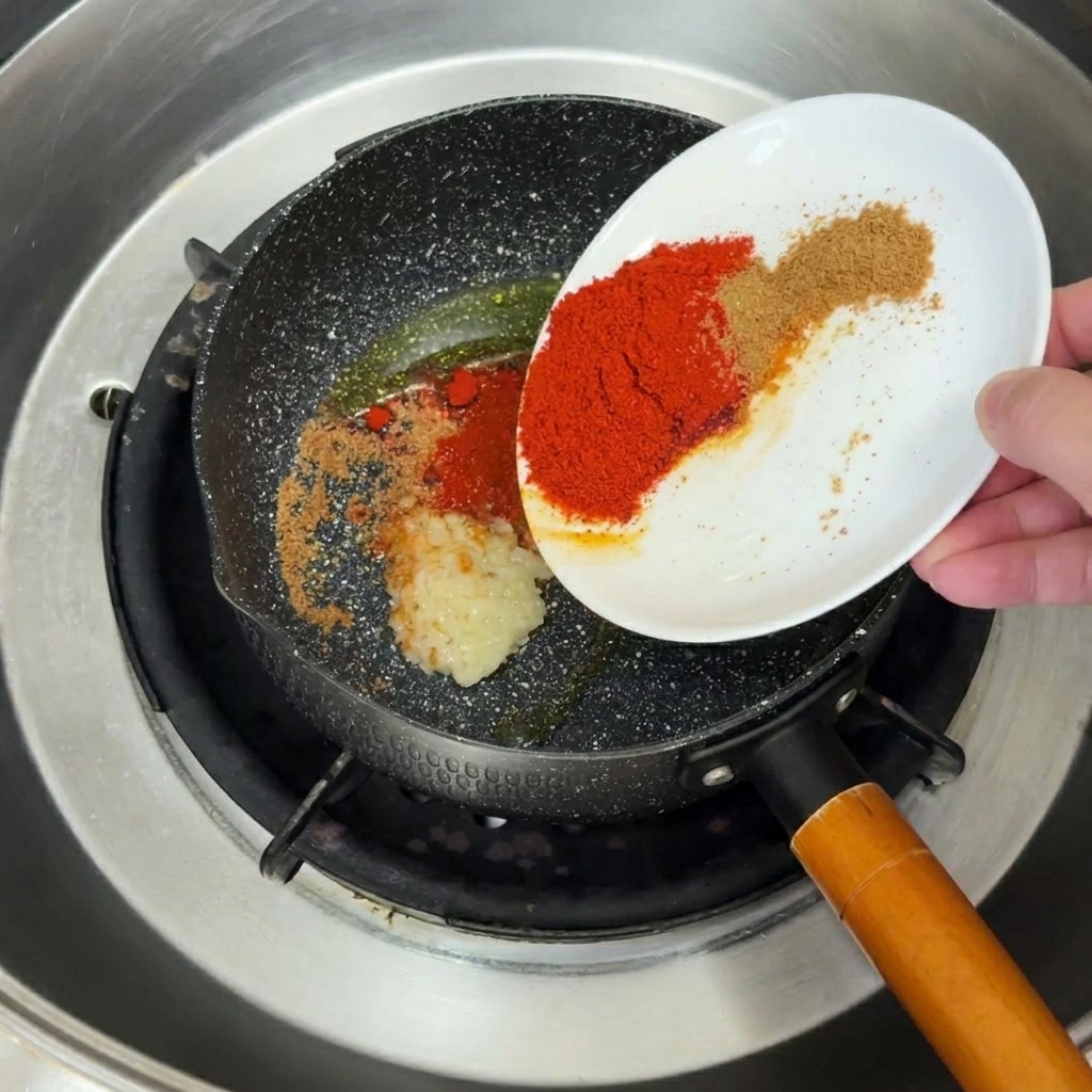 Ajo picado y especias friéndose y dorándose en aceite en una sartén negra.