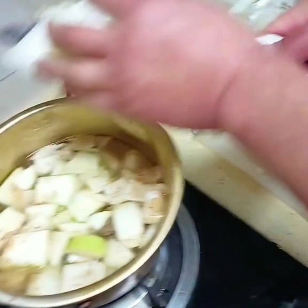 Hojas de col china cortadas colocándose en una olla de sopa a fuego lento con otras verduras.