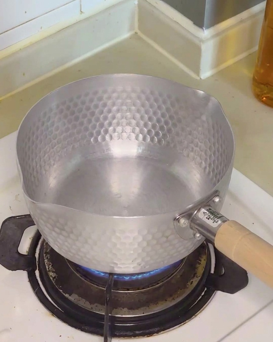 Agua vertida en una olla metálica sobre el fuego de una cocina de gas.