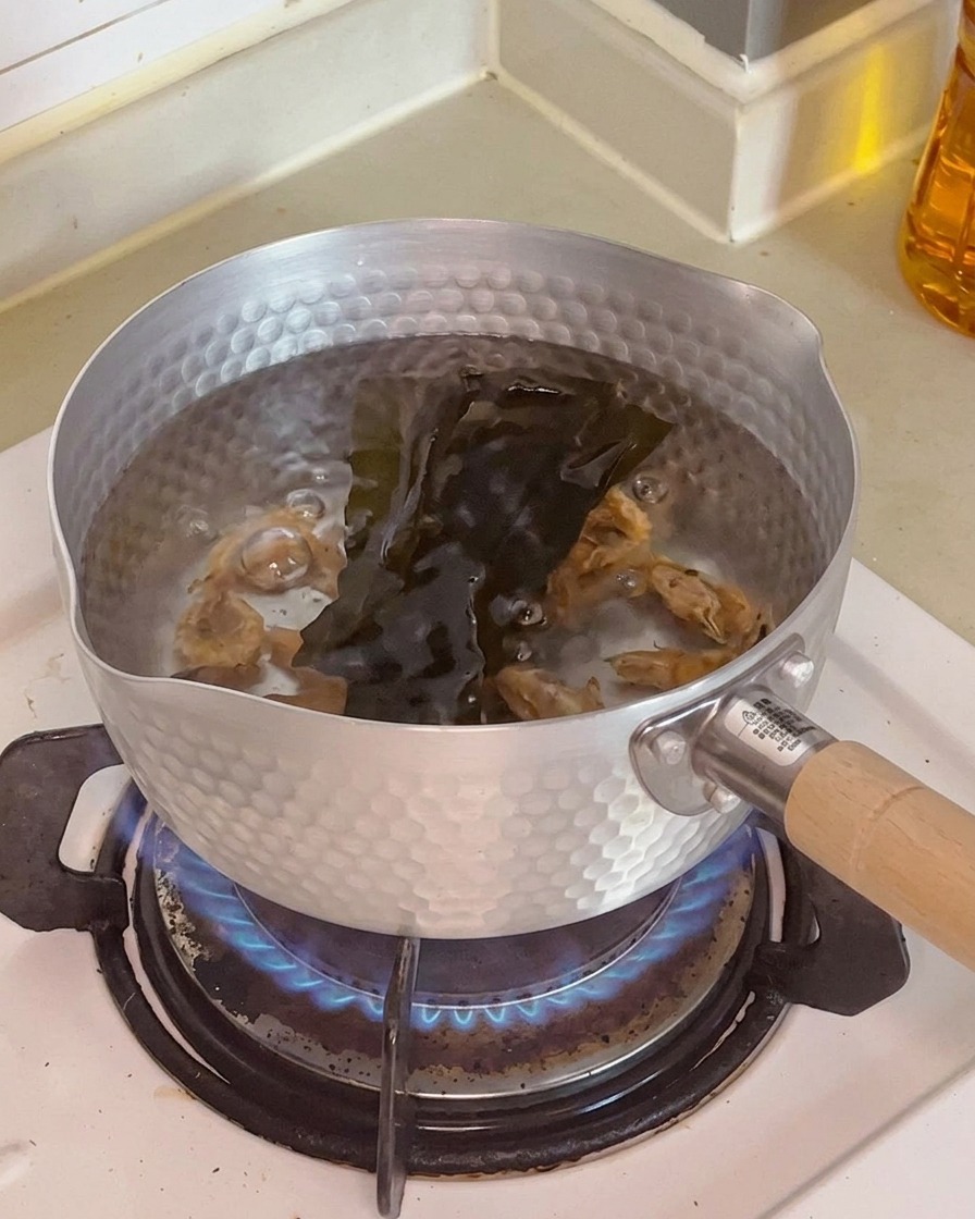Detalle de gambas secas y una lámina de alga kombu sumergidas en la olla con agua.