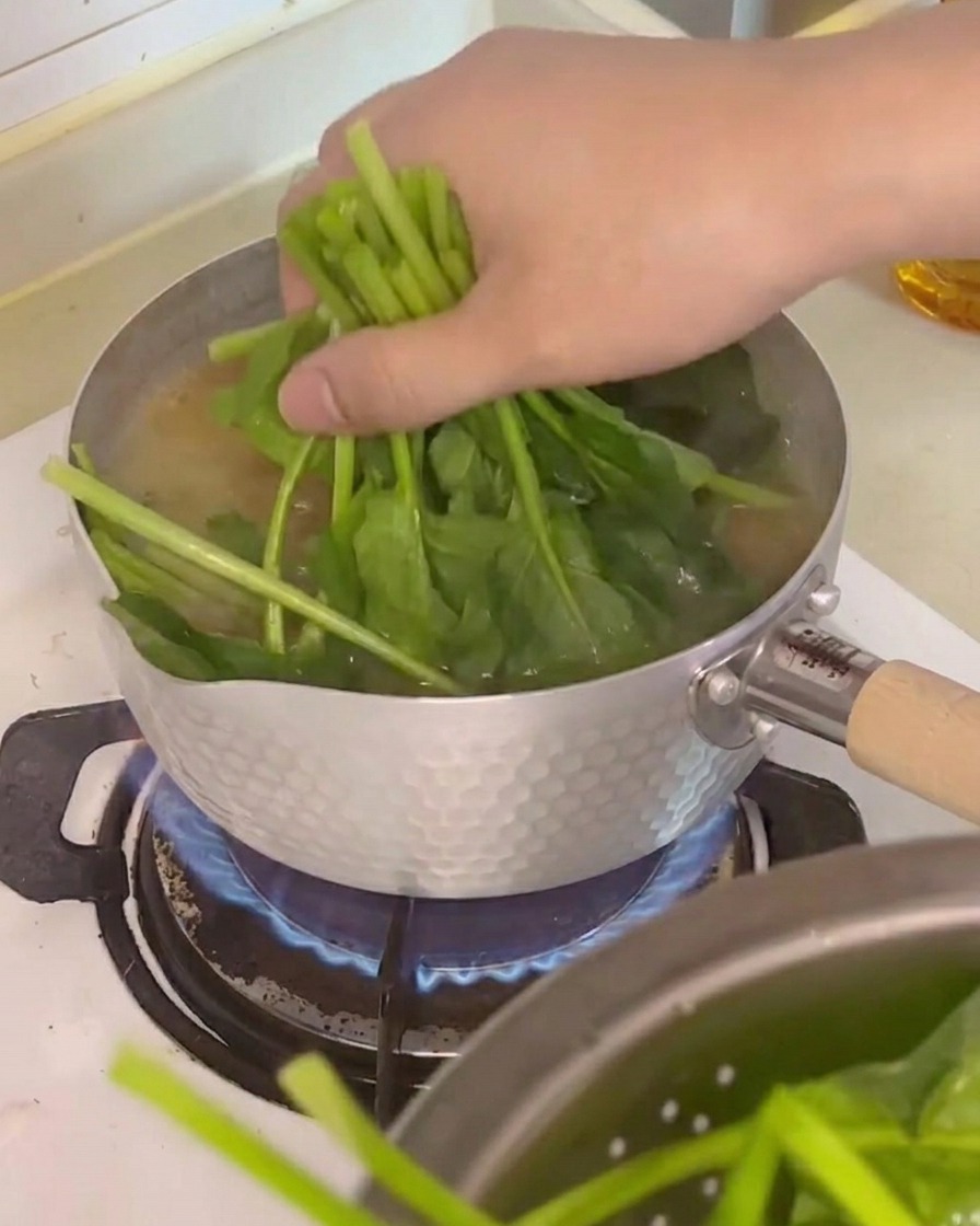 Espinacas, dados de tofu y setas enoki siendo añadidos a la olla con el caldo.