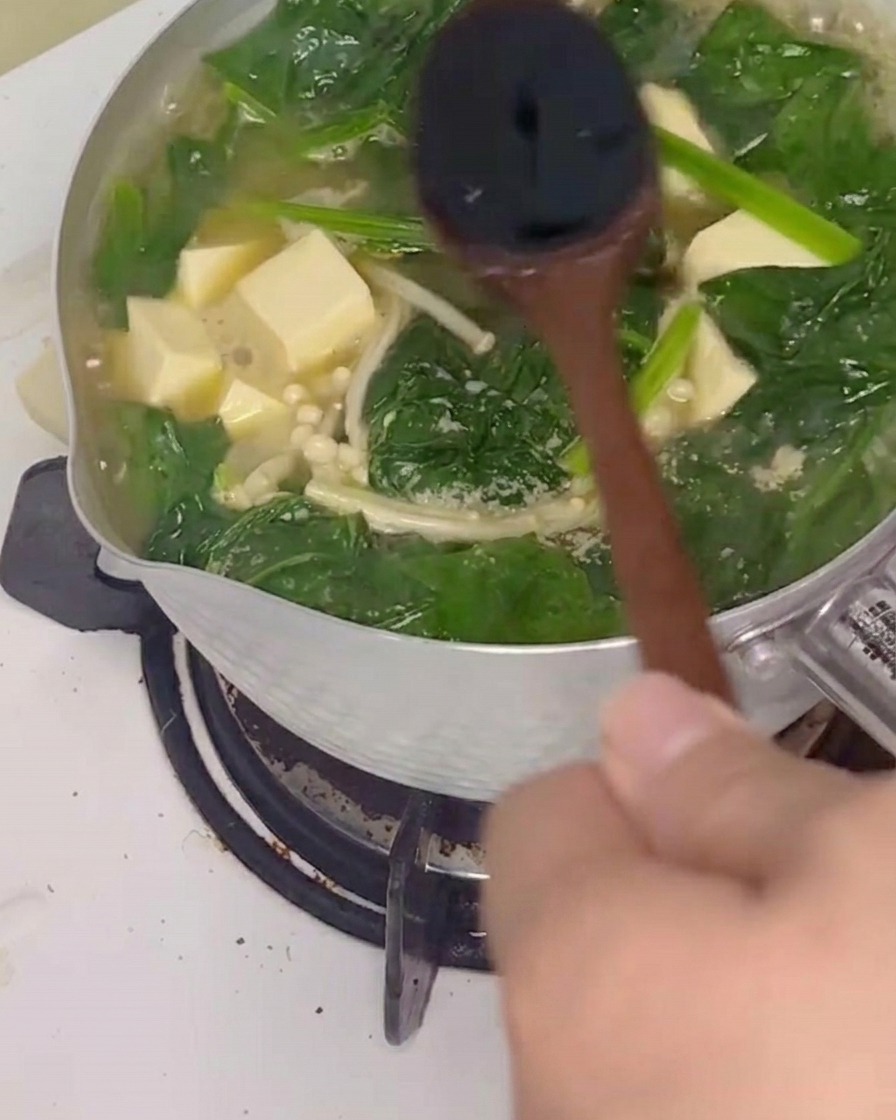 Salsa de soja siendo añadida a la sopa mientras se remueve con una cuchara de madera.