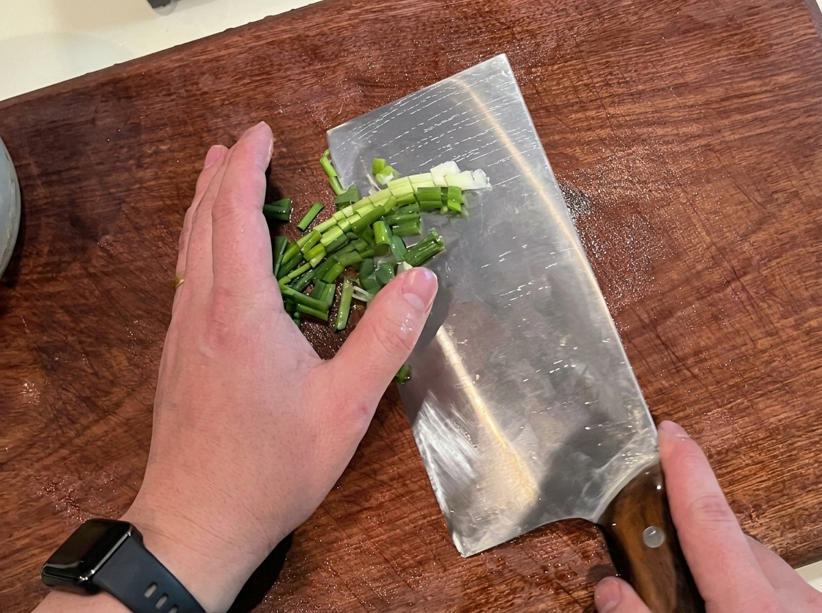 Cebolletas frescas siendo picadas finamente sobre una tabla de cortar de madera.