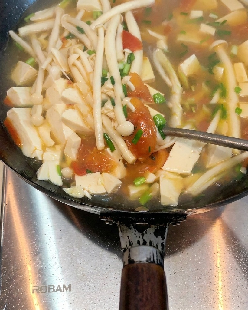 Tomates cocinándose en un wok con manteca derretida, empezando a ablandarse y soltar sus jugos.