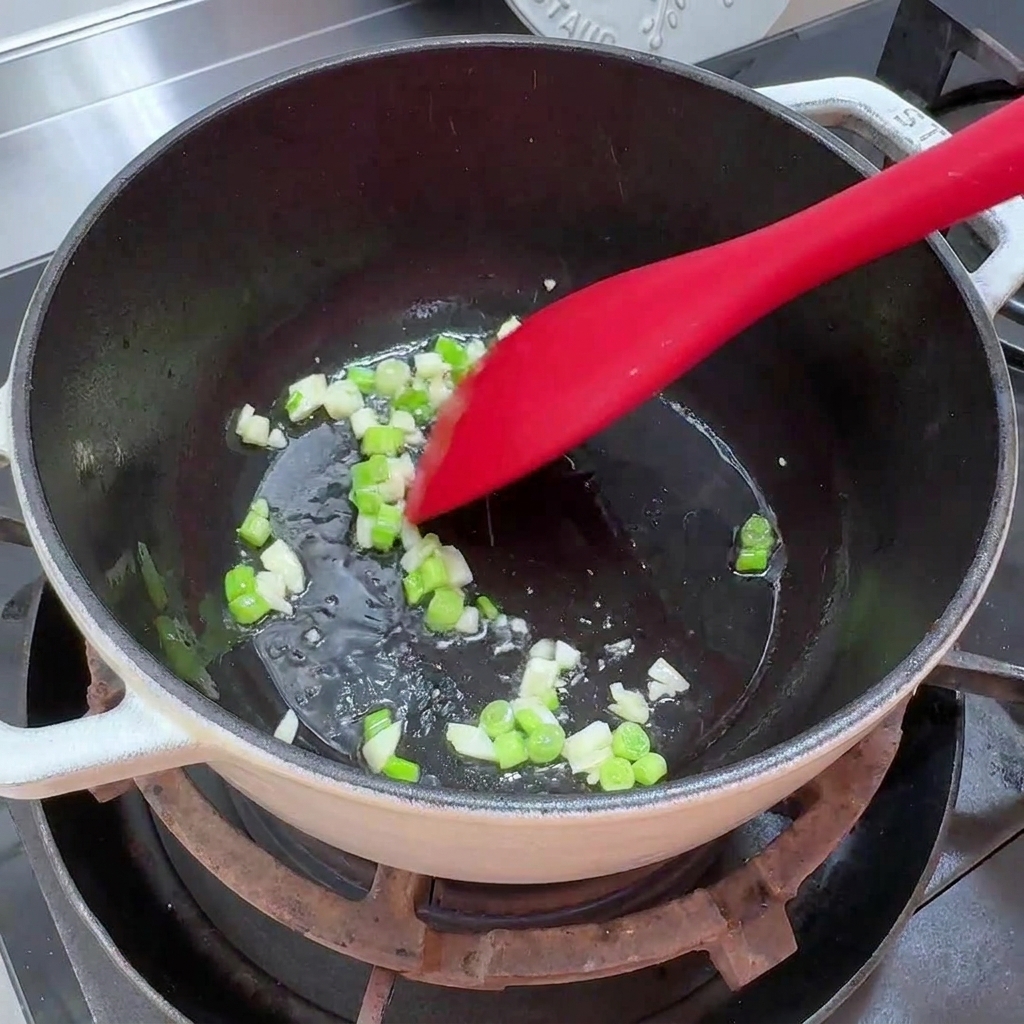 Cebollino picado y ajo picado chisporroteando en un poco de aceite en una olla.