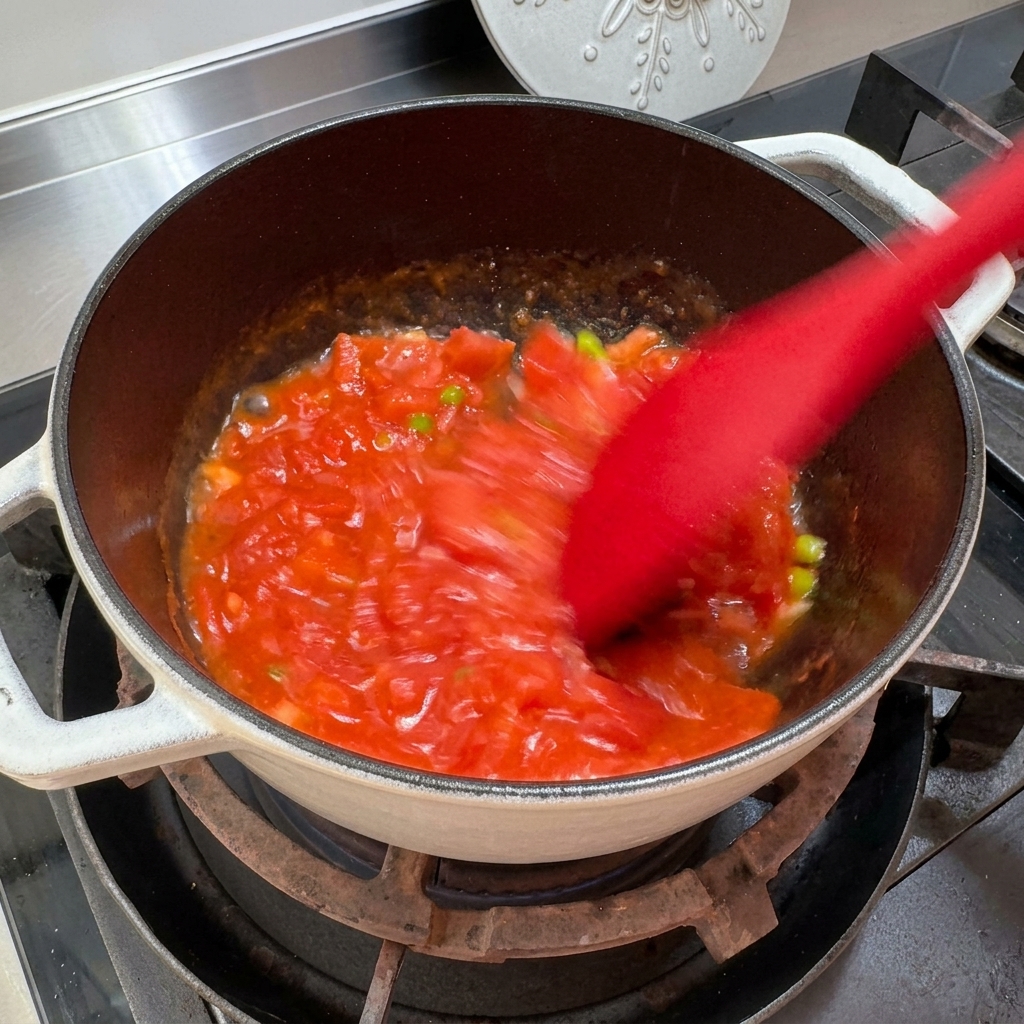 Tomates siendo aplastados y revueltos en una olla para crear una consistencia de salsa.