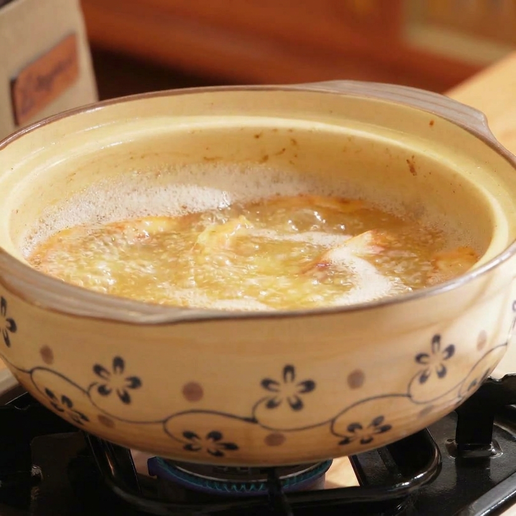 Una olla de barro llena de caldo hirviendo con tono anaranjado, con champiñones de marisco y shiitake siendo incorporados.
