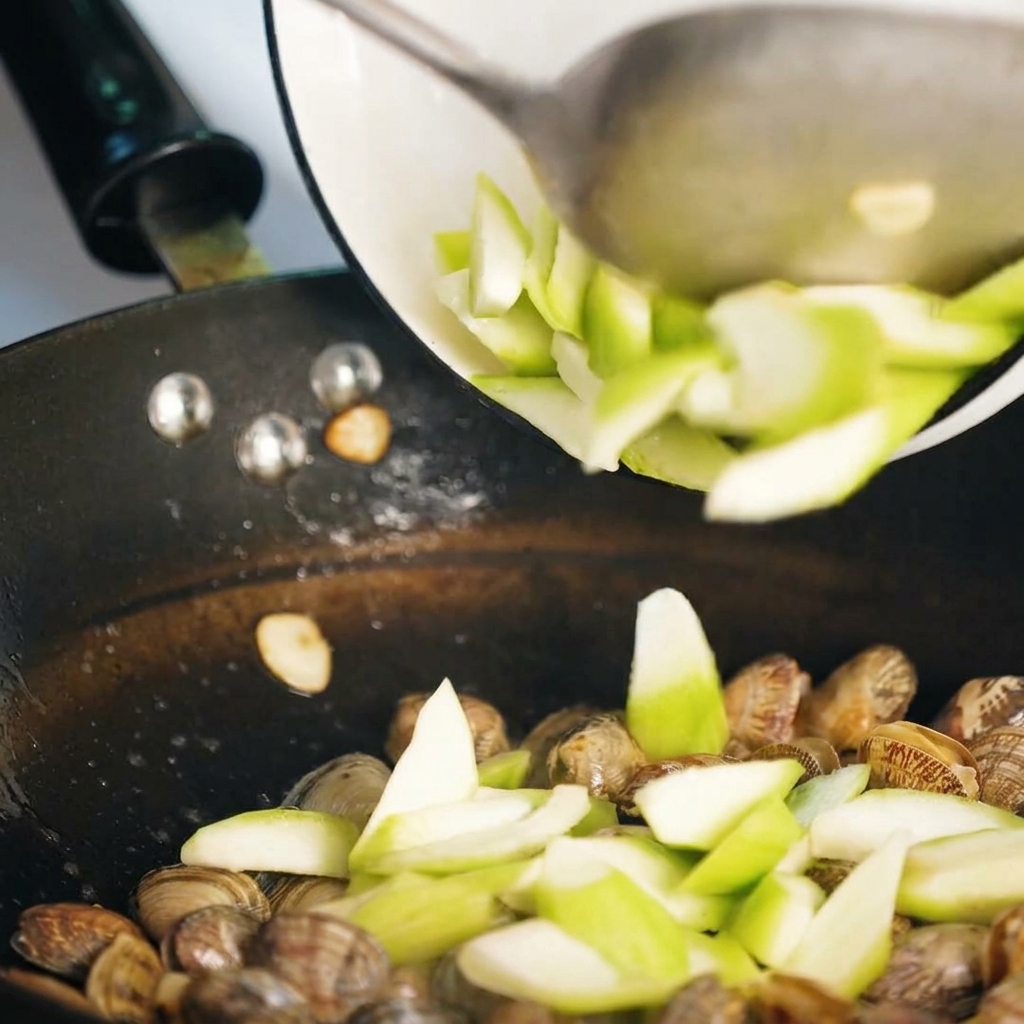 Rodajas de luffa siendo salteadas con almejas en la sartén.