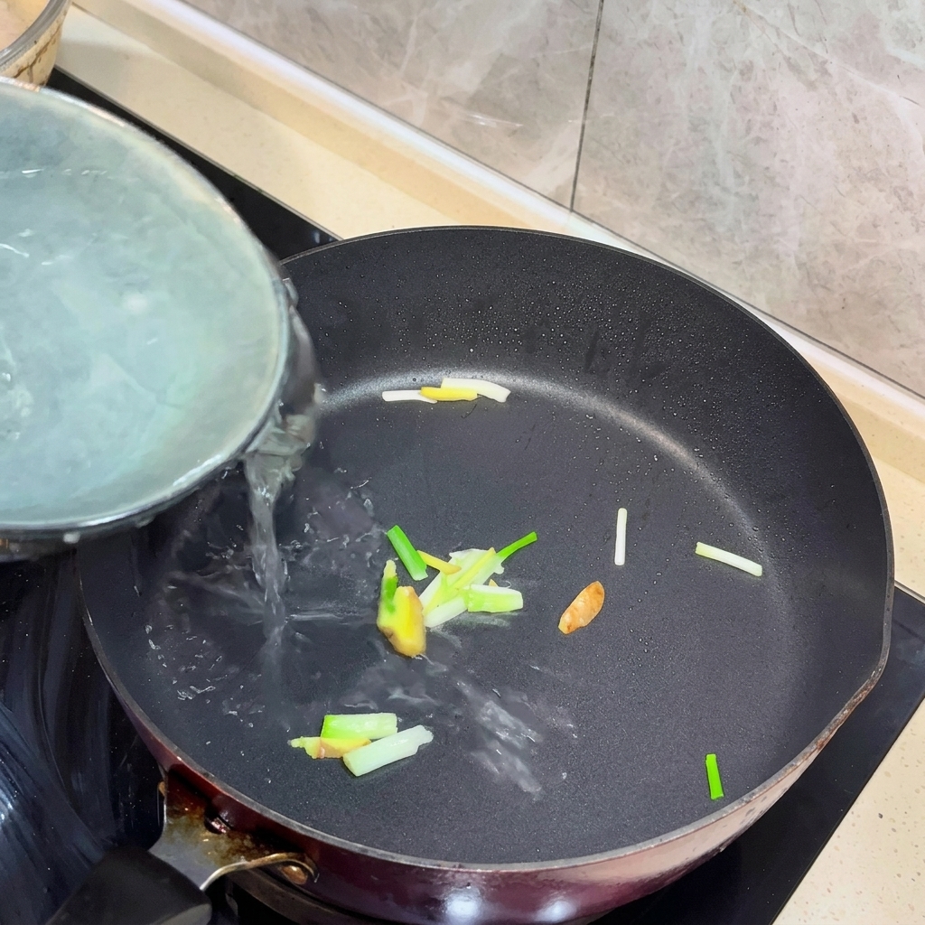 Agua hirviendo vertiéndose en una sartén con jengibre y cebollino salteados.