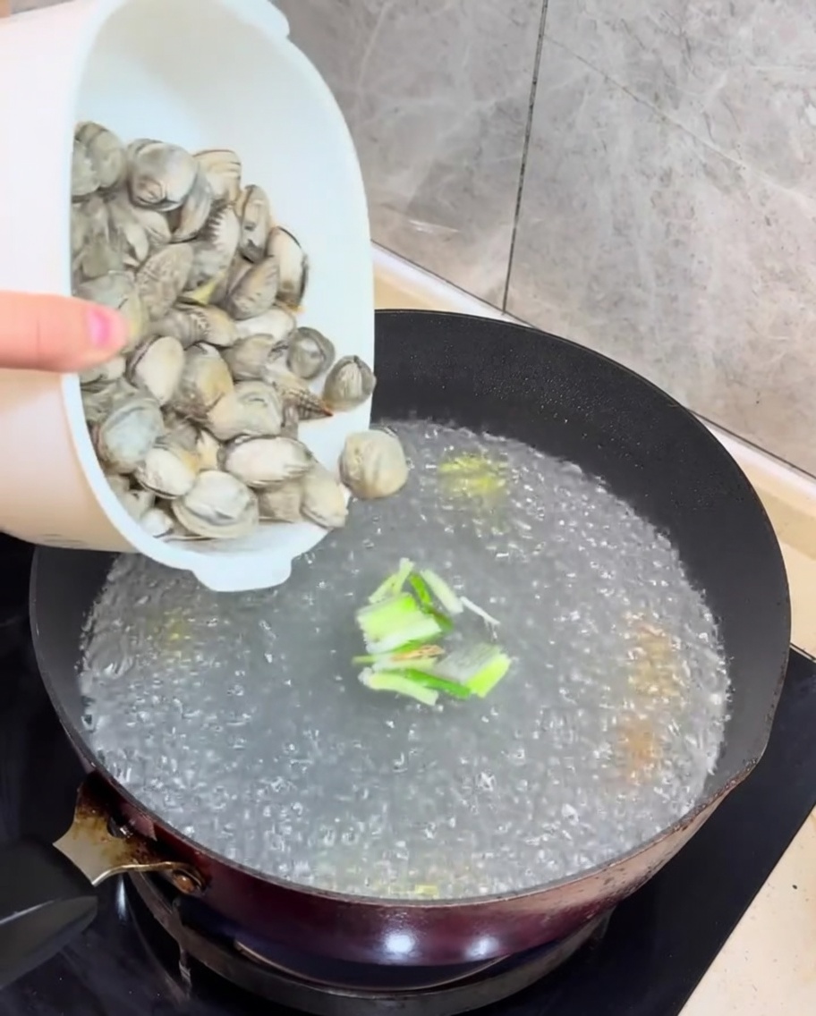 Almejas frescas y cubos de tofu siendo añadidos al caldo hirviendo.