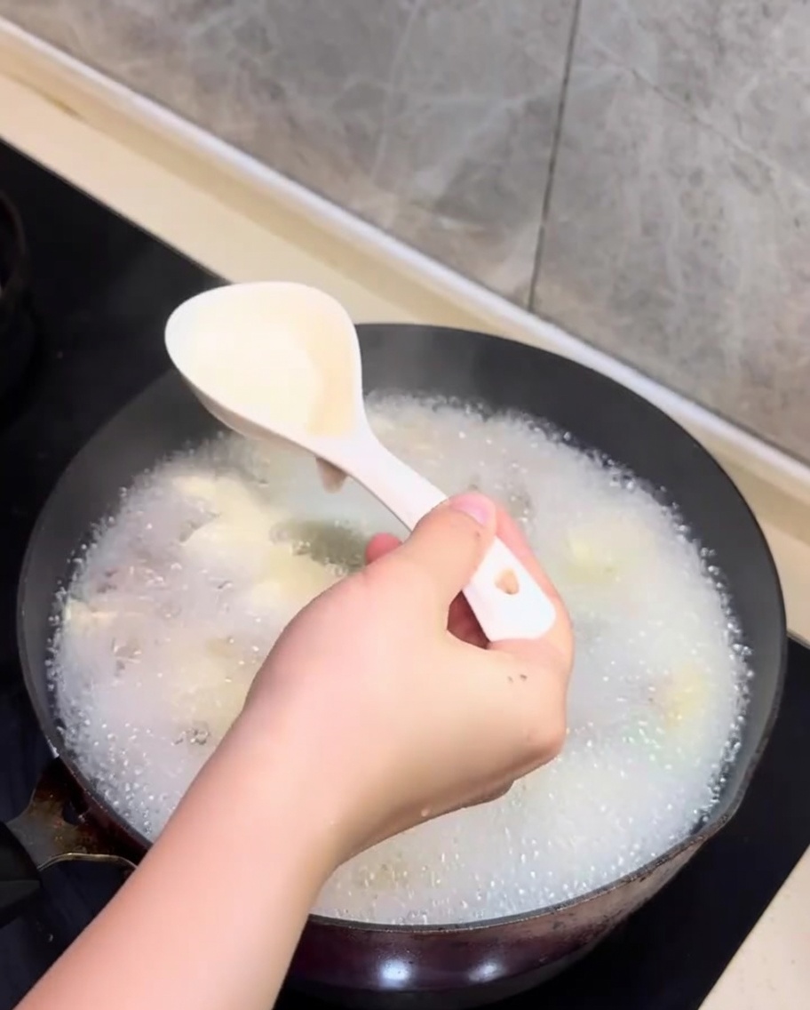 Una cuchara retirando la espuma blanca de la superficie de la sopa de almejas y tofu.