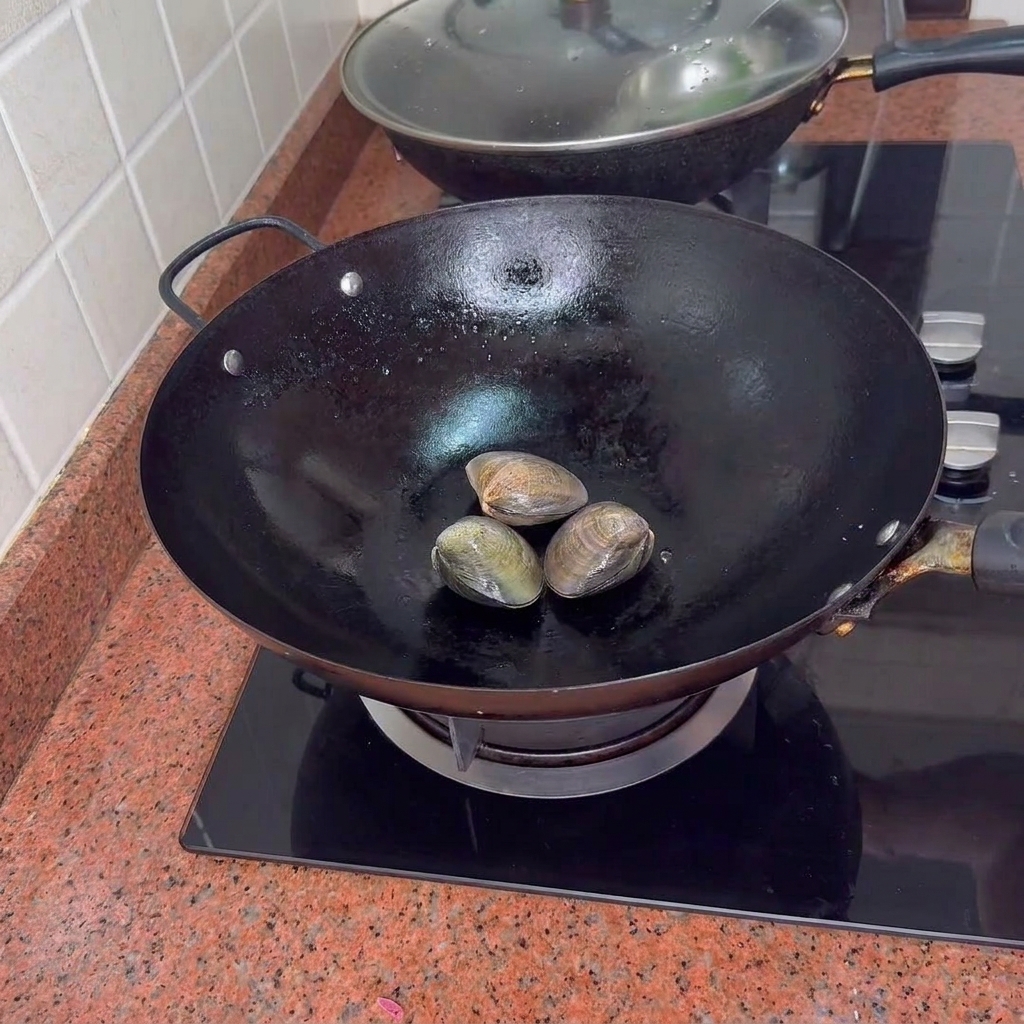 Tres almejas cerradas en un wok negro sobre la estufa.