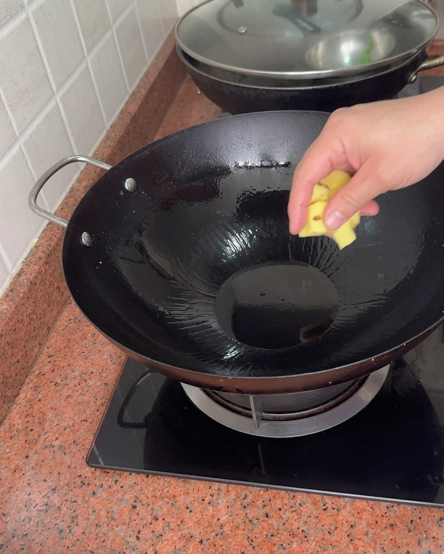 Una mano dejando caer un trozo de jengibre en un wok caliente con aceite.