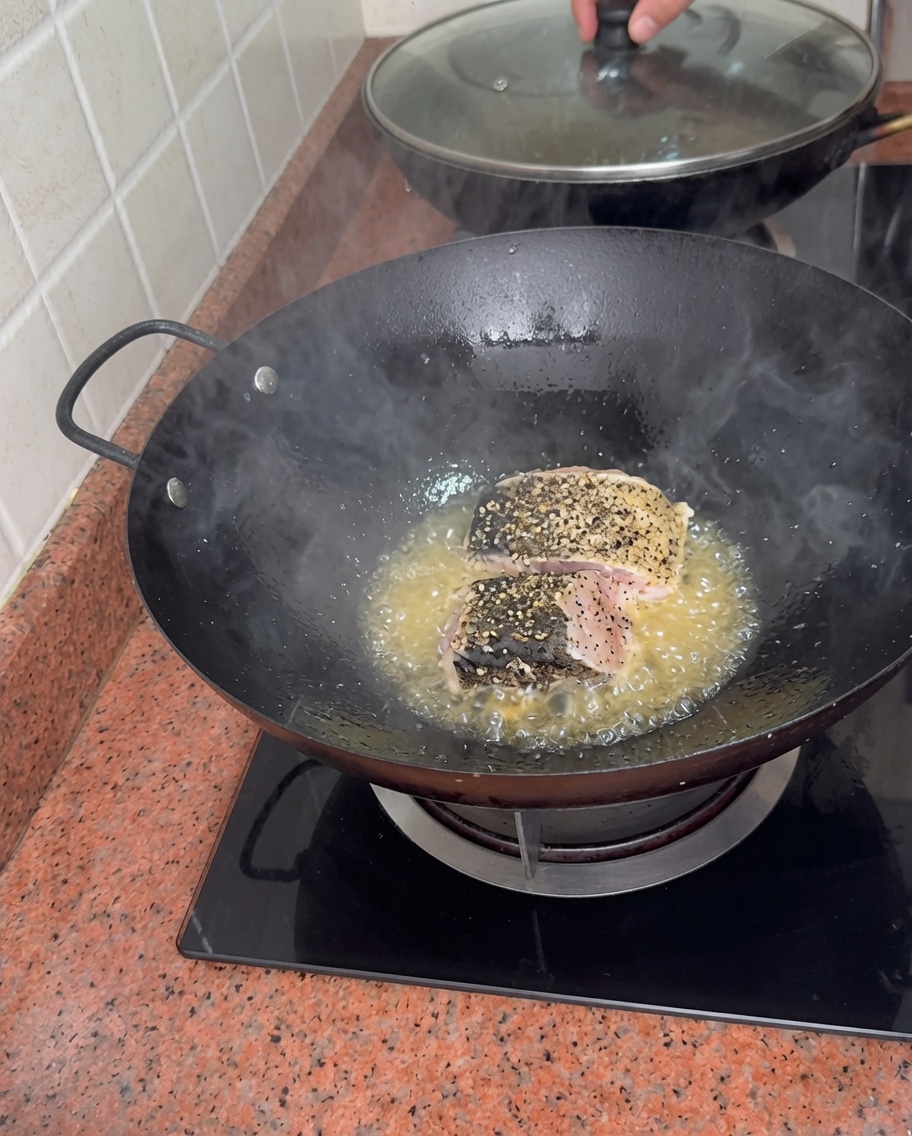 Trozos gruesos de mero sazonado sellándose en aceite burbujeante en un wok.