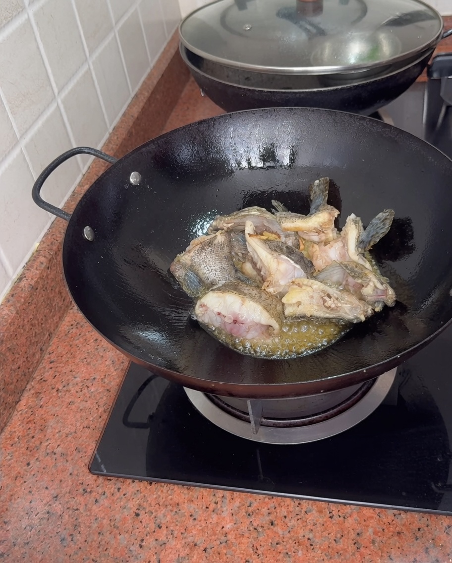 Trozos de mero hirviendo en un wok mientras se añade agua caliente, creando un caldo de pescado blanco y espeso.
