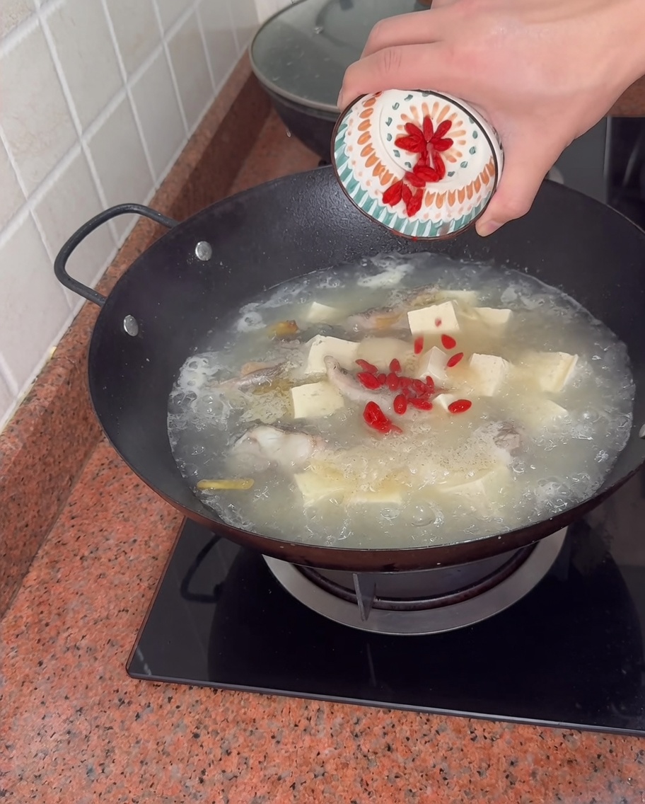 Añadiendo bayas de goji rojas desde un pequeño tazón a un wok burbujeante de sopa.
