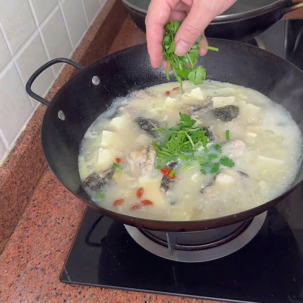 Una olla terminada de sopa de pescado, tofu y almejas decorada con cebollinos frescos.