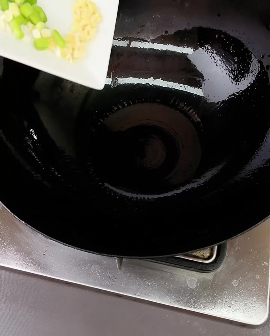 Cebolleta picada y ajo picado chisporroteando en un wok caliente con un poco de aceite.