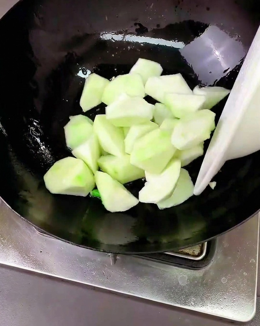 Trozos de luffa siendo salteados en un wok con los aromáticos.
