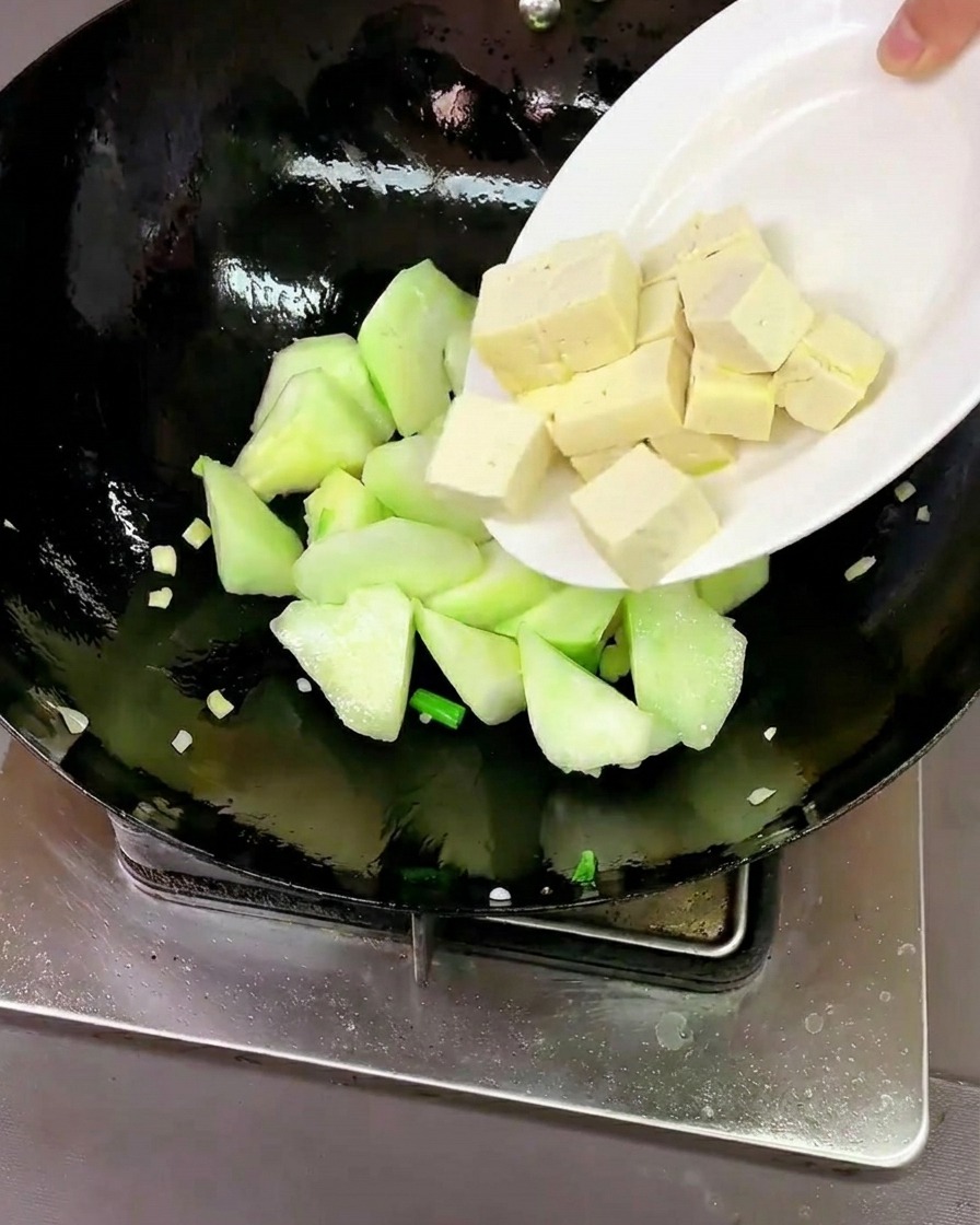 Cubos de tofu fresco y almejas crudas limpias siendo añadidas al wok con la luffa.
