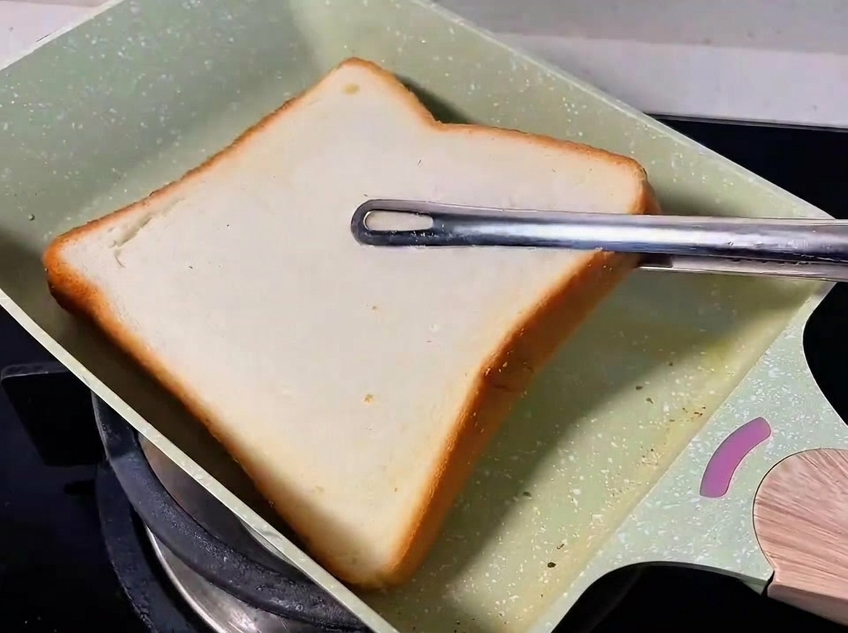Una rebanada de pan blanco tostándose en una sartén verde.