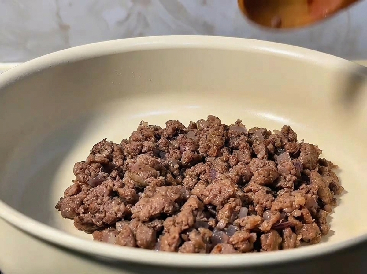 Carne picada siendo removida y desmenuzada en una sartén con cebolla salteada.