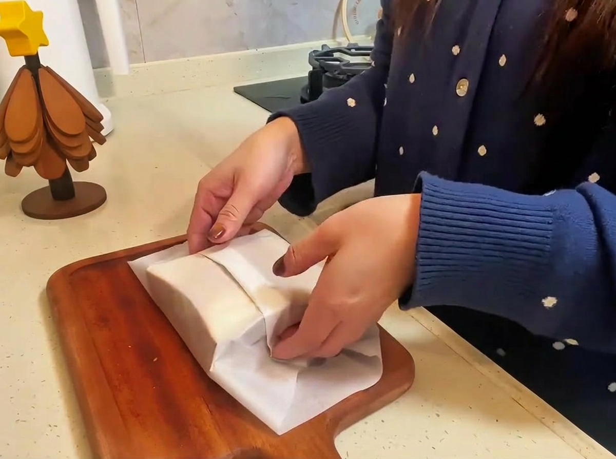 El sándwich de ternera y queso terminado, envuelto en papel de horno y siendo cortado por la mitad sobre una tabla de madera.