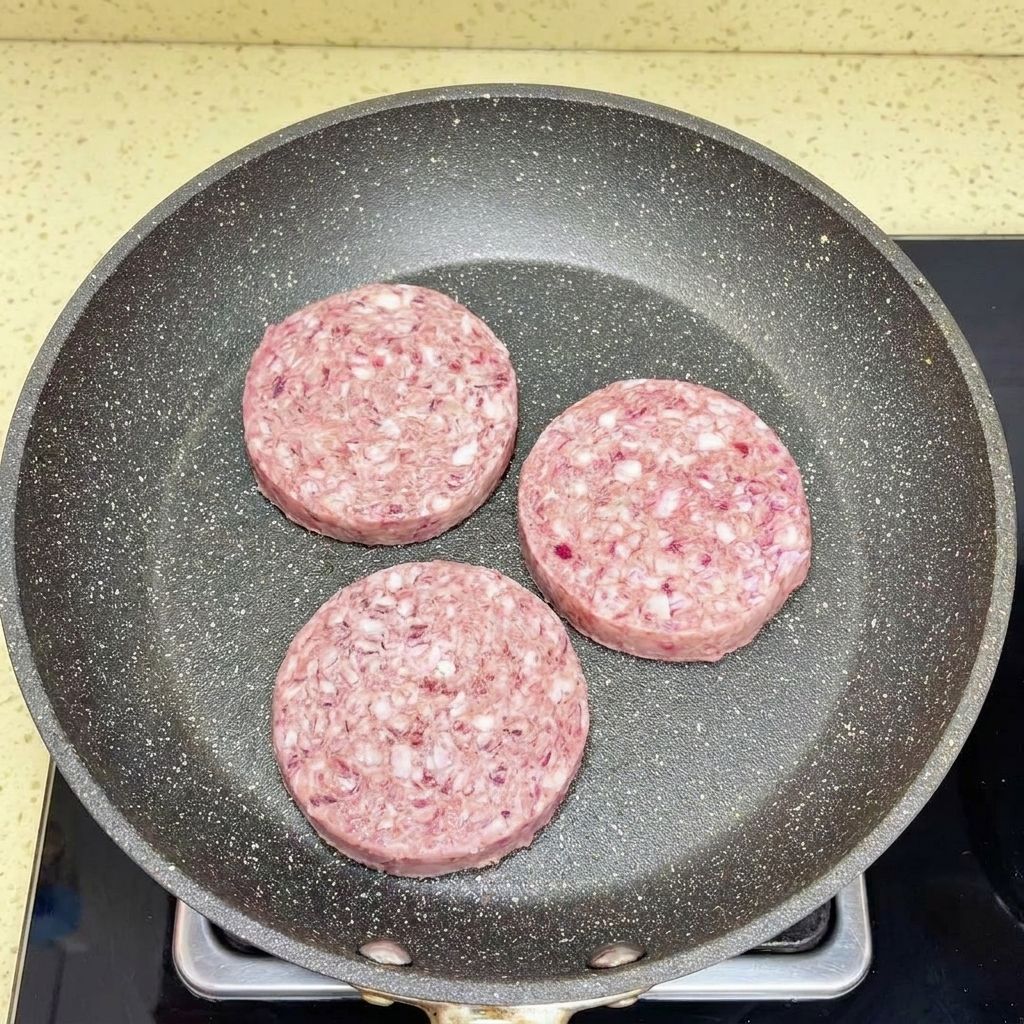 Ternera picada siendo desmenuzada en una sartén caliente con una espátula blanca.