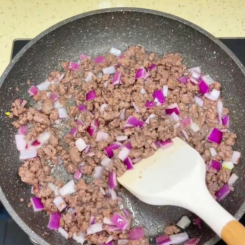 Ternera picada salteada y cebolla roja picada siendo sazonadas con salsas en una sartén.