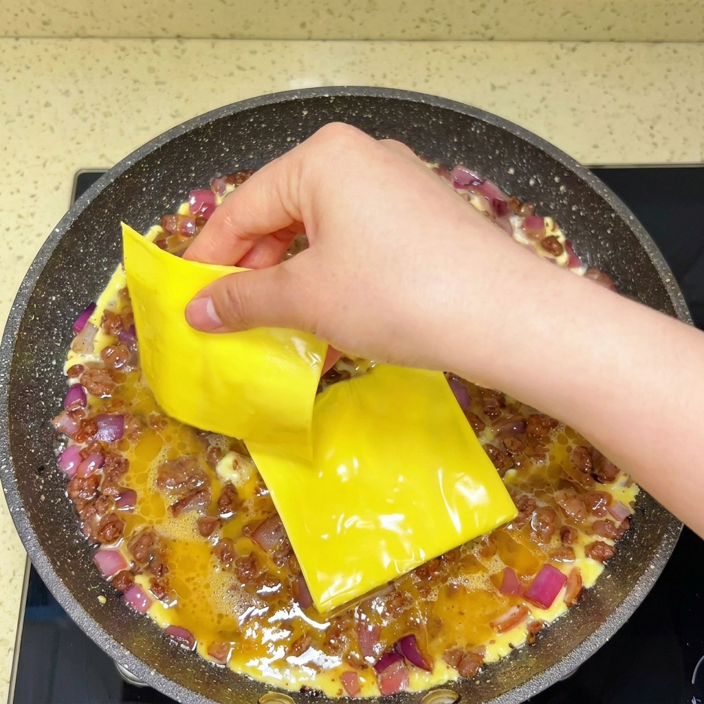 Lonchas de queso procesado colocadas sobre los huevos y la ternera en la sartén.