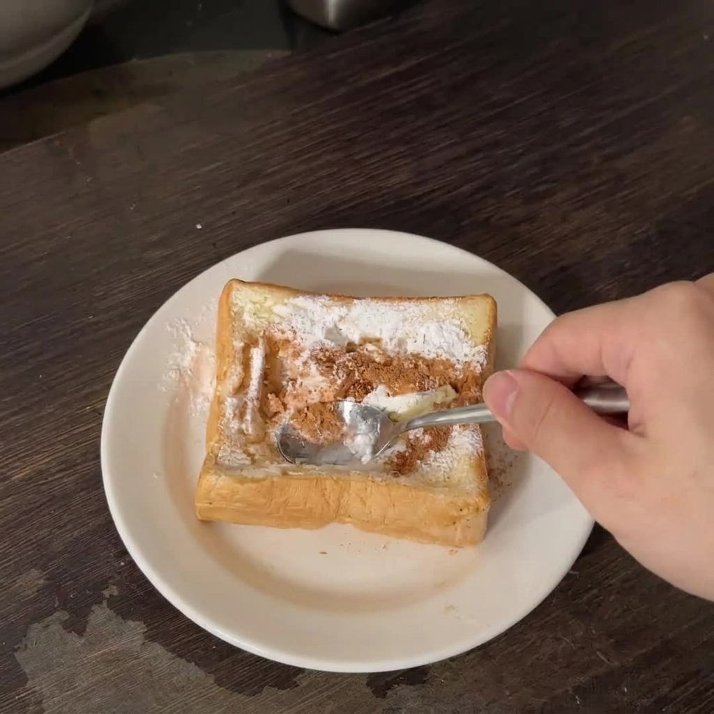 Una mano usando una cuchara de metal para presionar el centro de una rebanada gruesa de pan blanco sobre un plato blanco.