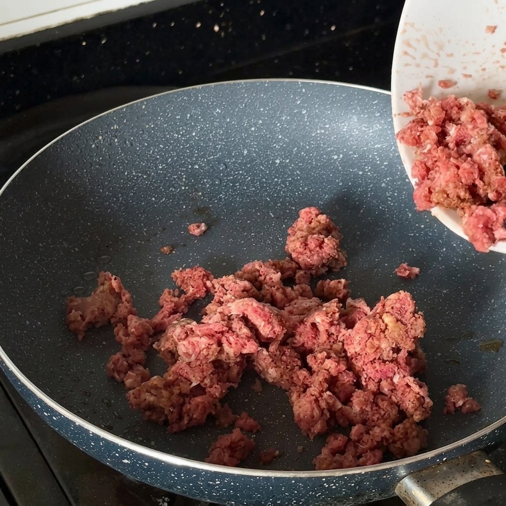 Carne molida sazonada dorándose en una sartén caliente.