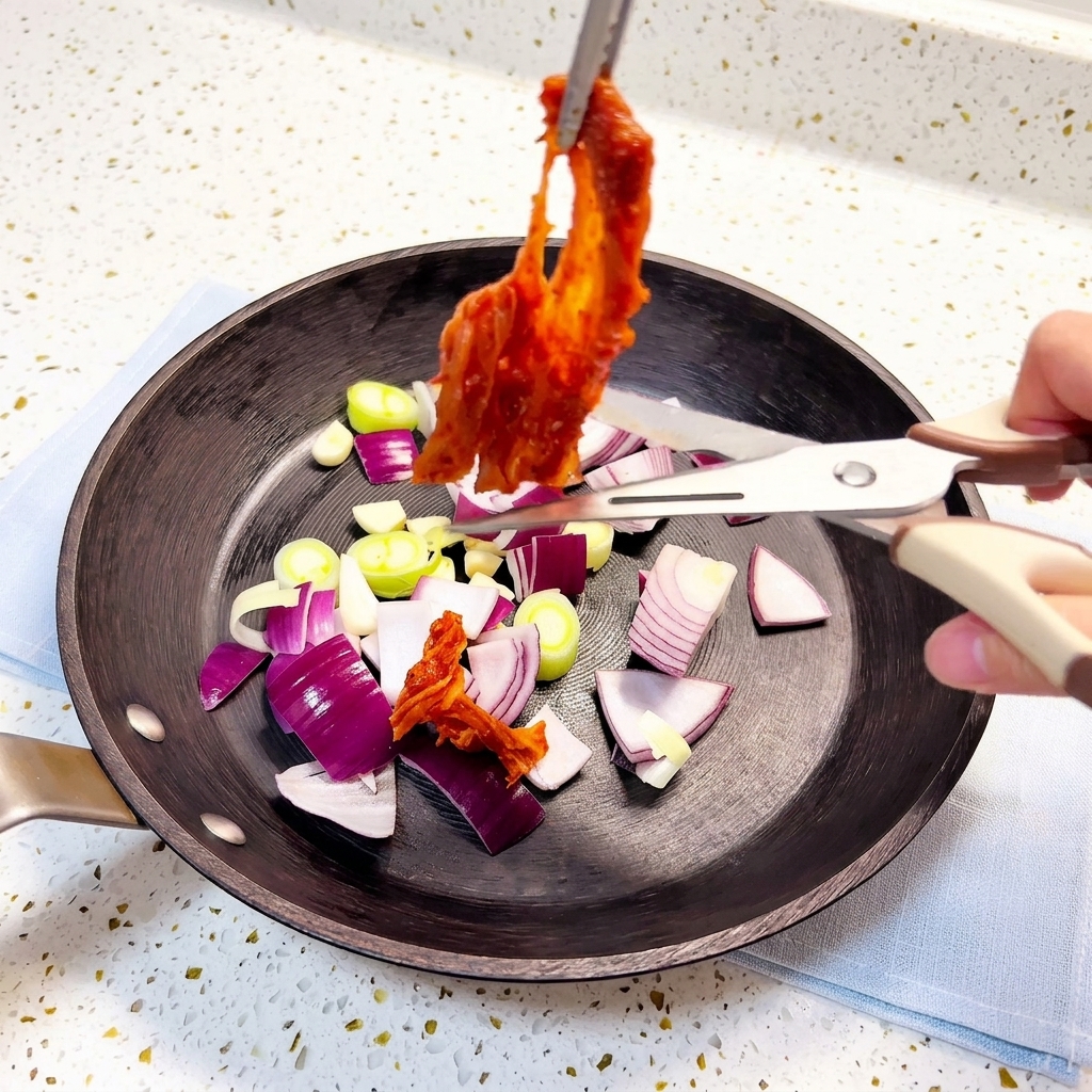 Kimchi siendo cortado con tijeras de cocina directamente sobre una sartén.