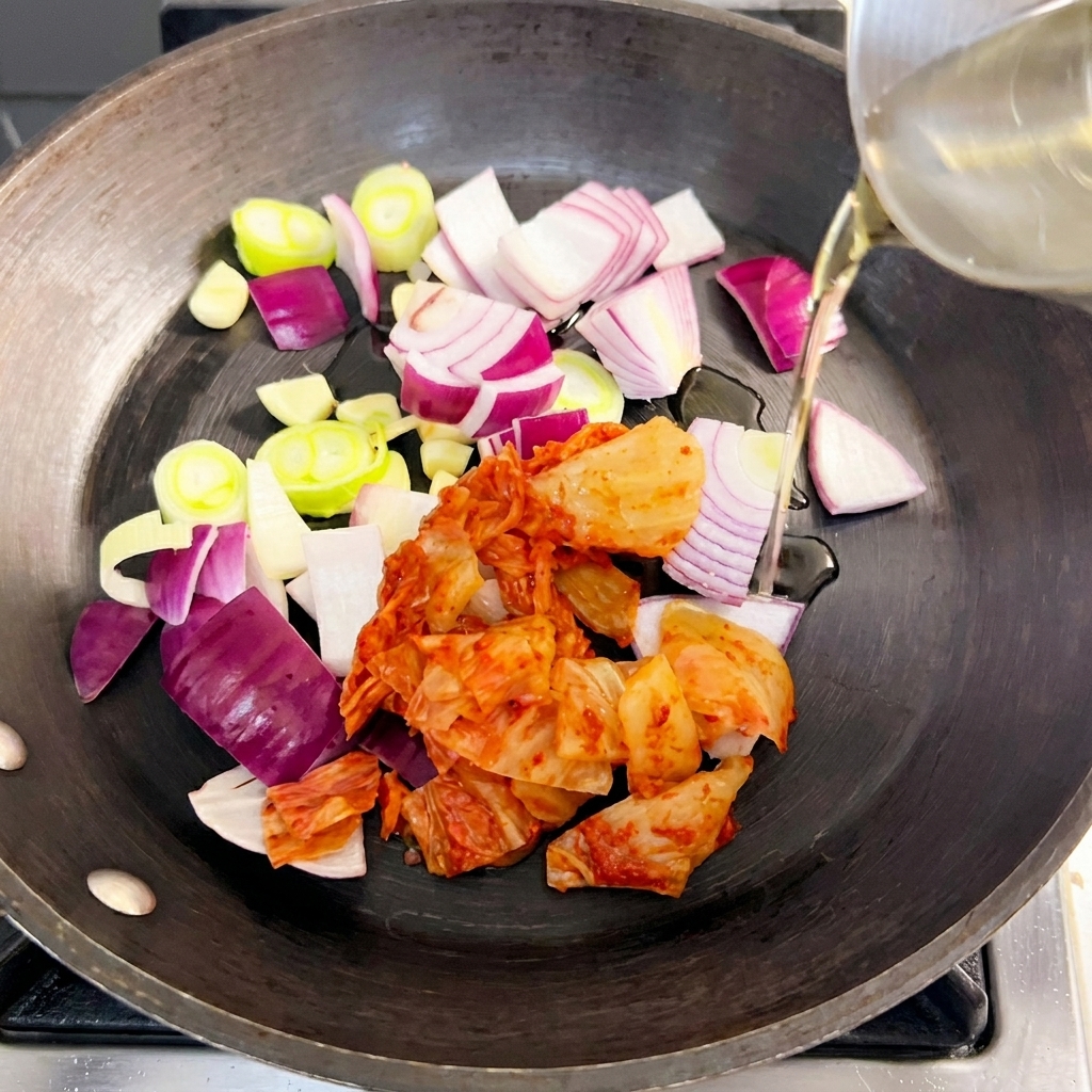 Sartén con cebolla, cebolleta y kimchi salteándose en aceite.