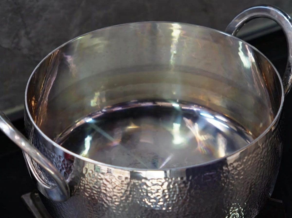 Vista cercana de aceite vertiéndose en una olla de acero inoxidable brillante.