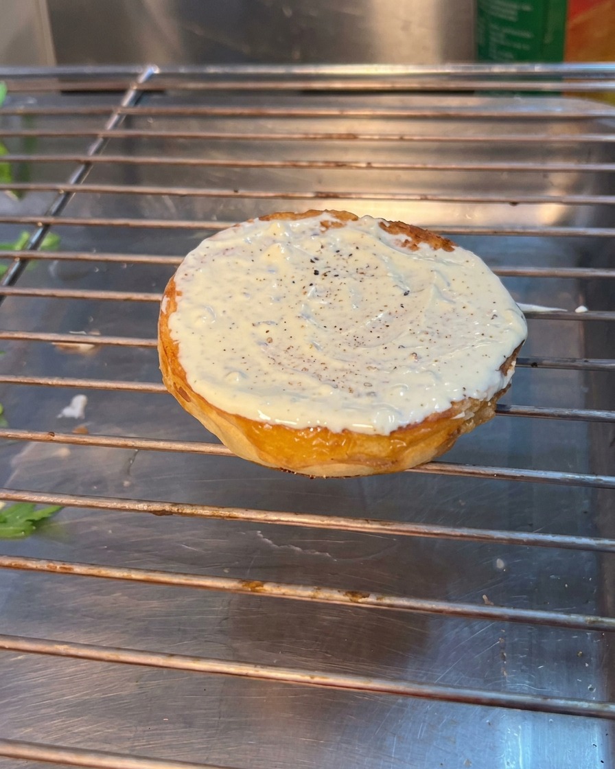 Montaje de hamburguesa mostrando rúcula, tomate y pepinillos colocados sobre el pan inferior.