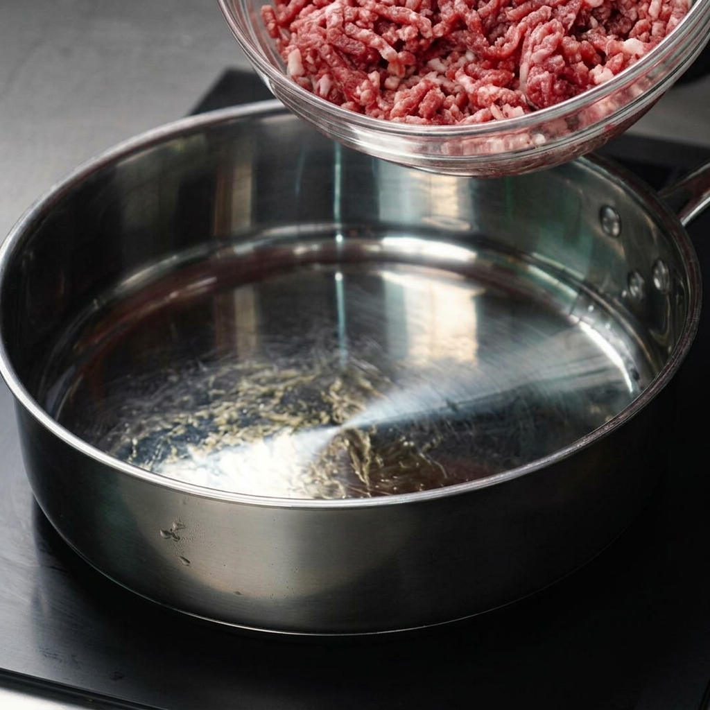 Carne molida trasladándose de un bol de vidrio a una sartén caliente.