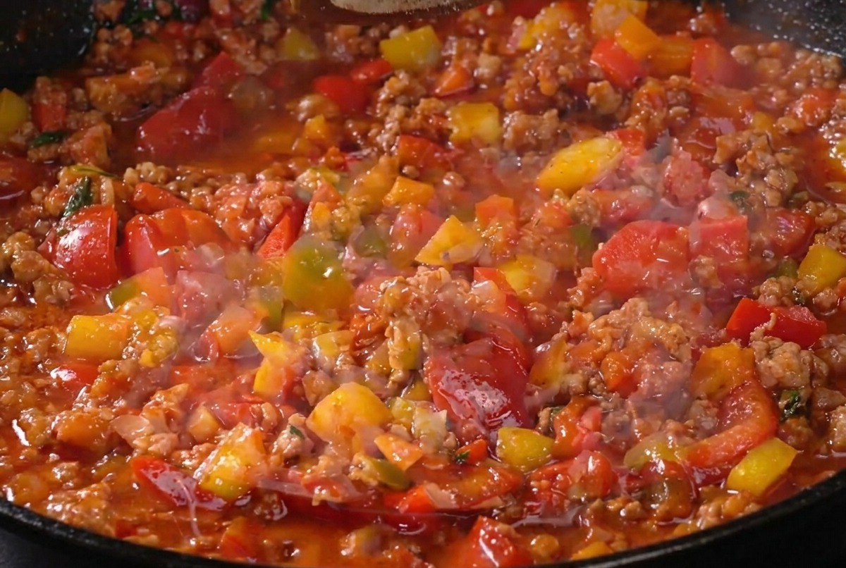 La salsa de carne cocinándose a fuego lento en la sartén mientras se sazona con pimienta, mostrando una textura rica y espesa.