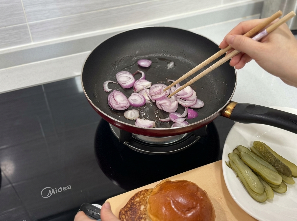 Tiras de cebolla morada salteándose en una sartén caliente con palillos de madera.