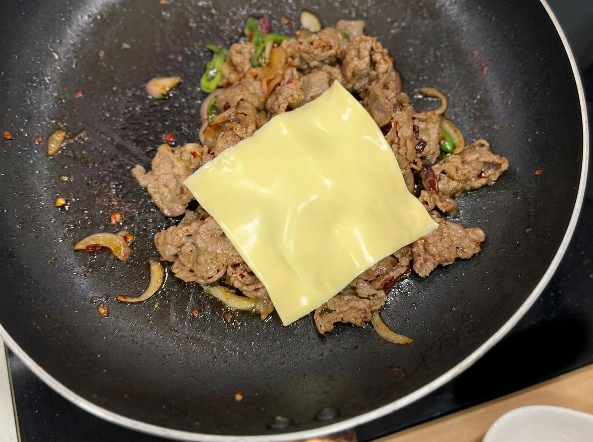 Una loncha de queso amarillo fundiéndose sobre la mezcla de ternera y cebolla en la sartén.