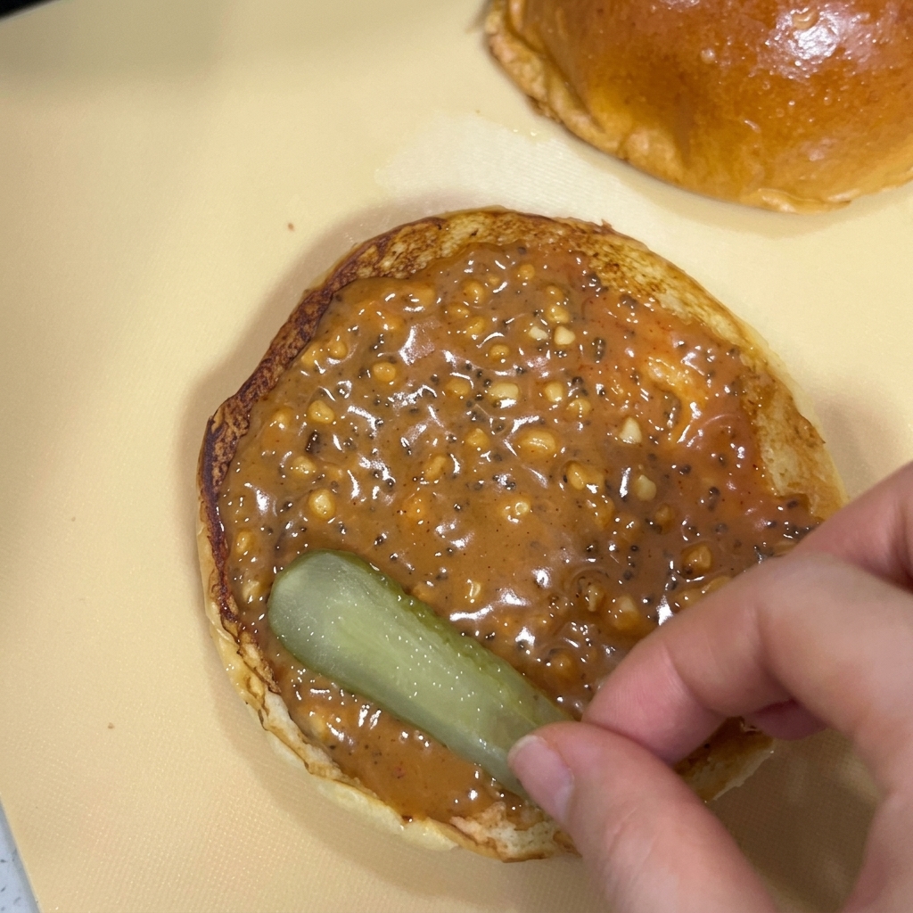 Una mano colocando una rodaja de pepinillo sobre el pan con salsa de cacahuete.