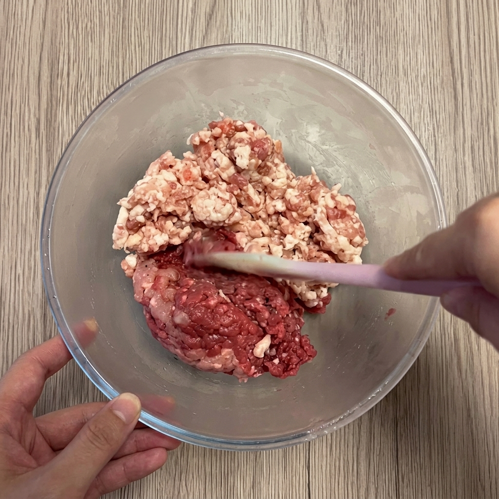 Carne de cerdo y ternera combinándose en un bol de mezcla transparente.