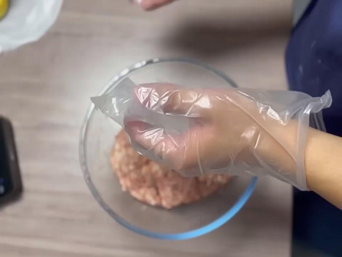 Manos enguantadas dando forma a una porción de carne hasta crear una bola firme y suave.