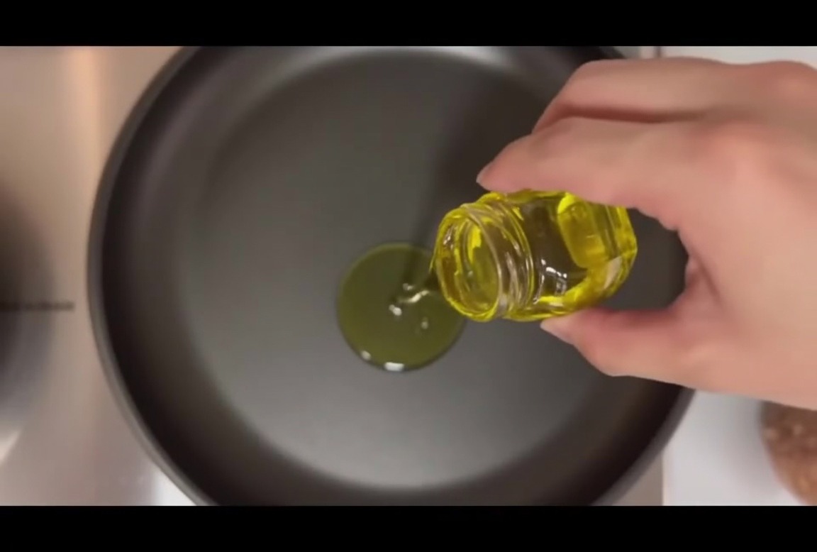 Cuatro hamburguesas crudas en una sartén caliente con aceite de oliva y dientes de ajo enteros.