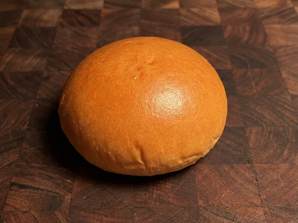 Un pan de hamburguesa tostado de color marrón dorado sobre una superficie de madera.