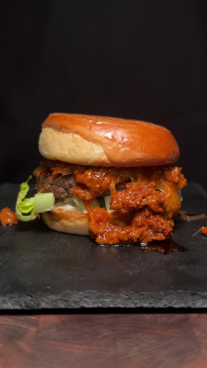 Una hamburguesa de Choriqueso gourmet con una gruesa pieza de carne de res y salsa de queso con chorizo sobre un pan tostado.